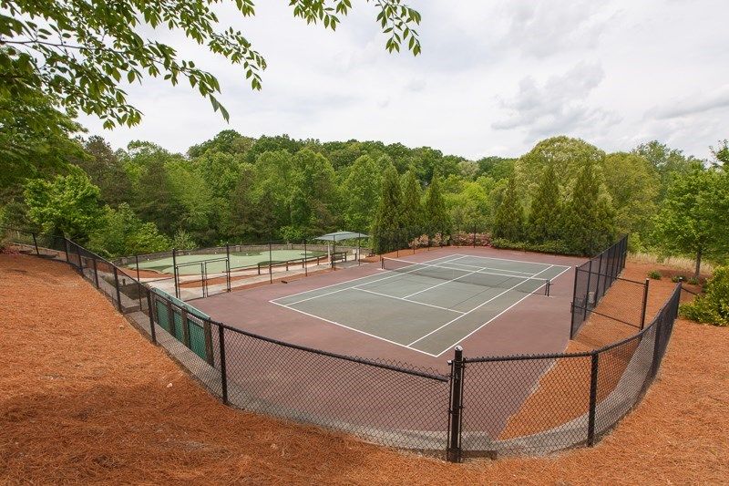 An outdoor tennis court surrounded by greenery and enclosed with a fence.