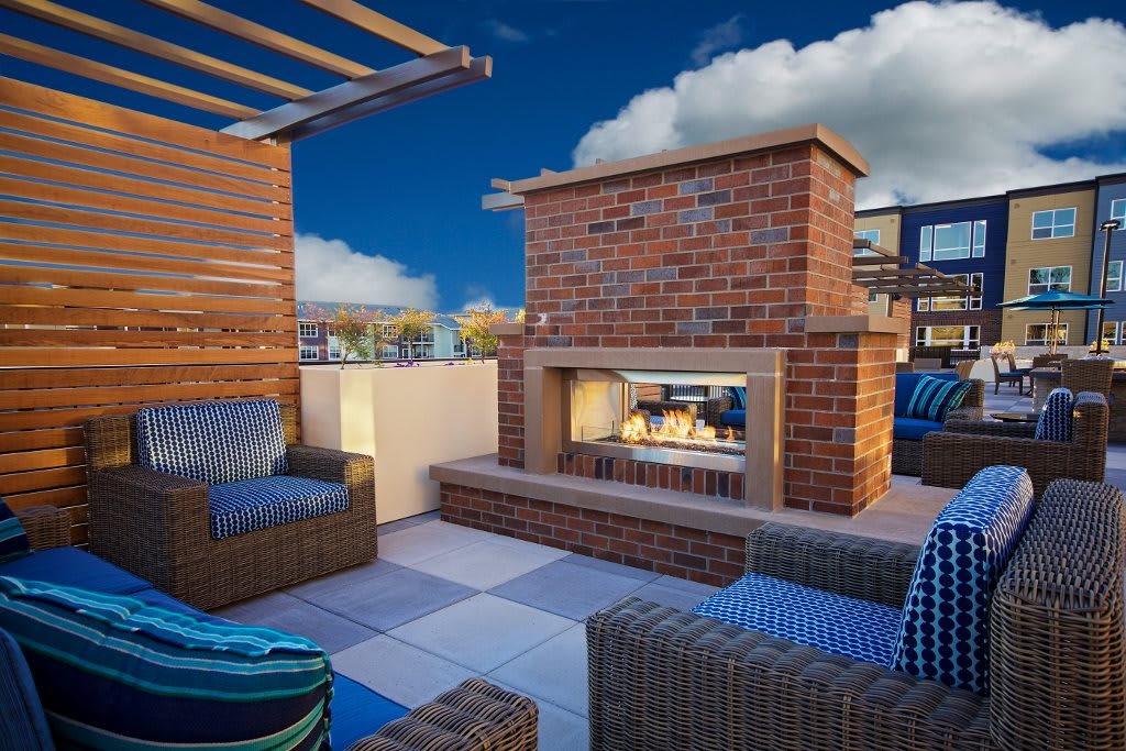 A cozy rooftop patio with a brick fireplace and comfortable outdoor seating under a clear evening sky.