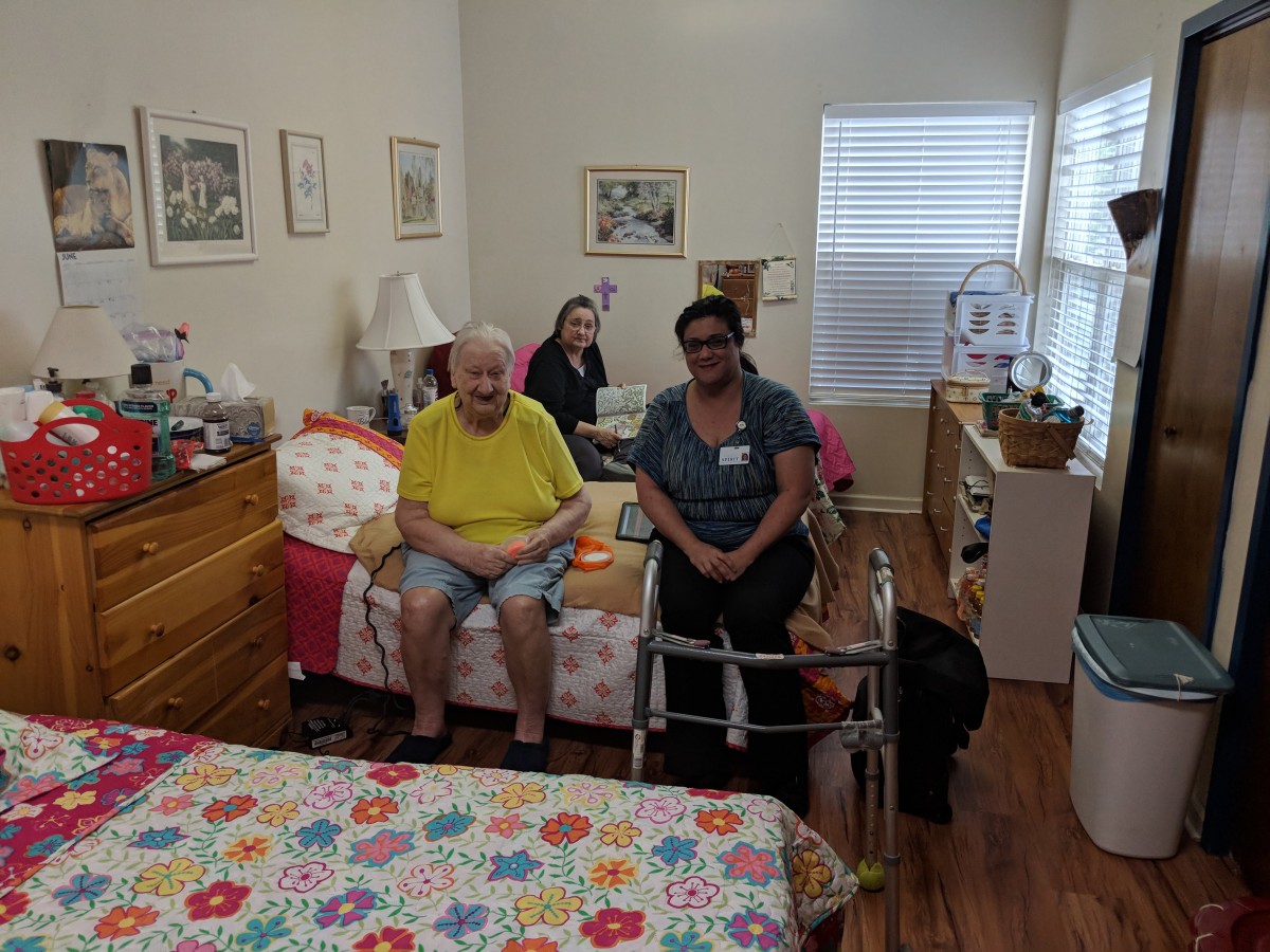 A group of people in a care facility room, with one using a walker.