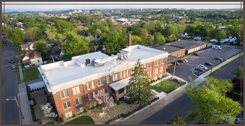 Aerial view of a brick building surrounded by greenery in an urban area.