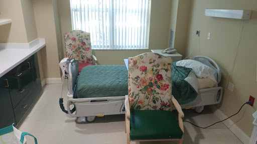 A patient room featuring a hospital bed and two floral-patterned chairs.