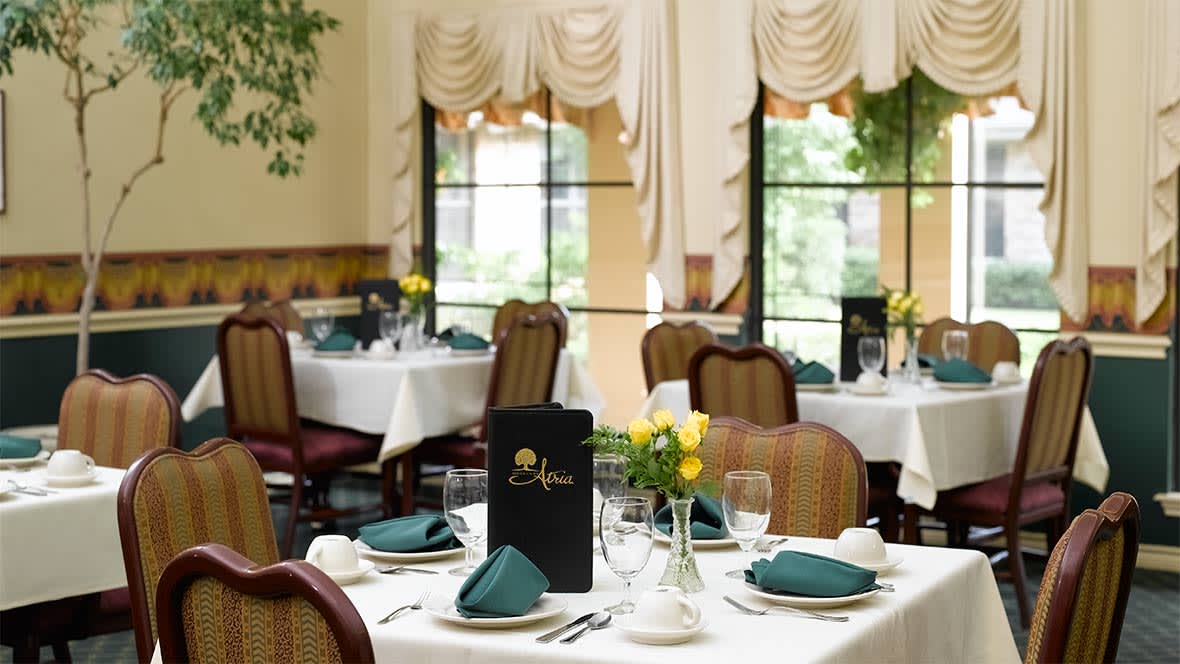 An elegant restaurant dining room with neatly set tables featuring green napkins and yellow flowers.