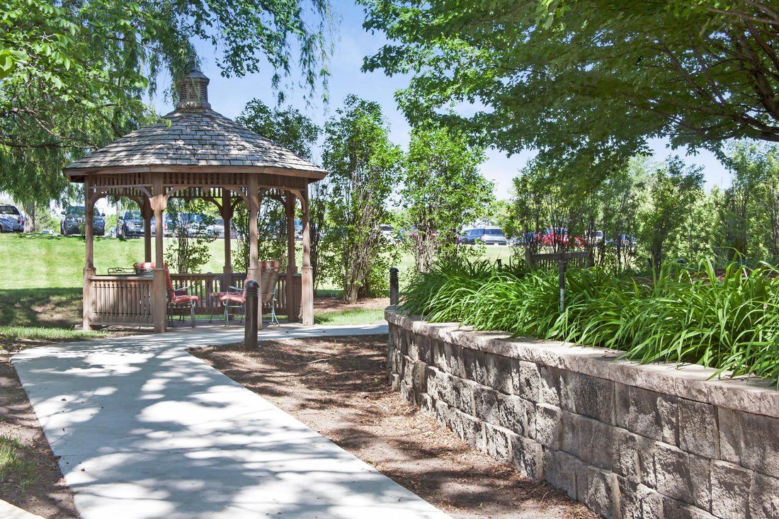 A tranquil park scene featuring a gazebo, surrounded by lush greenery and shaded pathways.