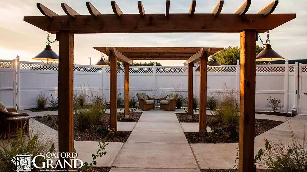 A serene garden pathway featuring a wooden pergola and cozy outdoor seating.