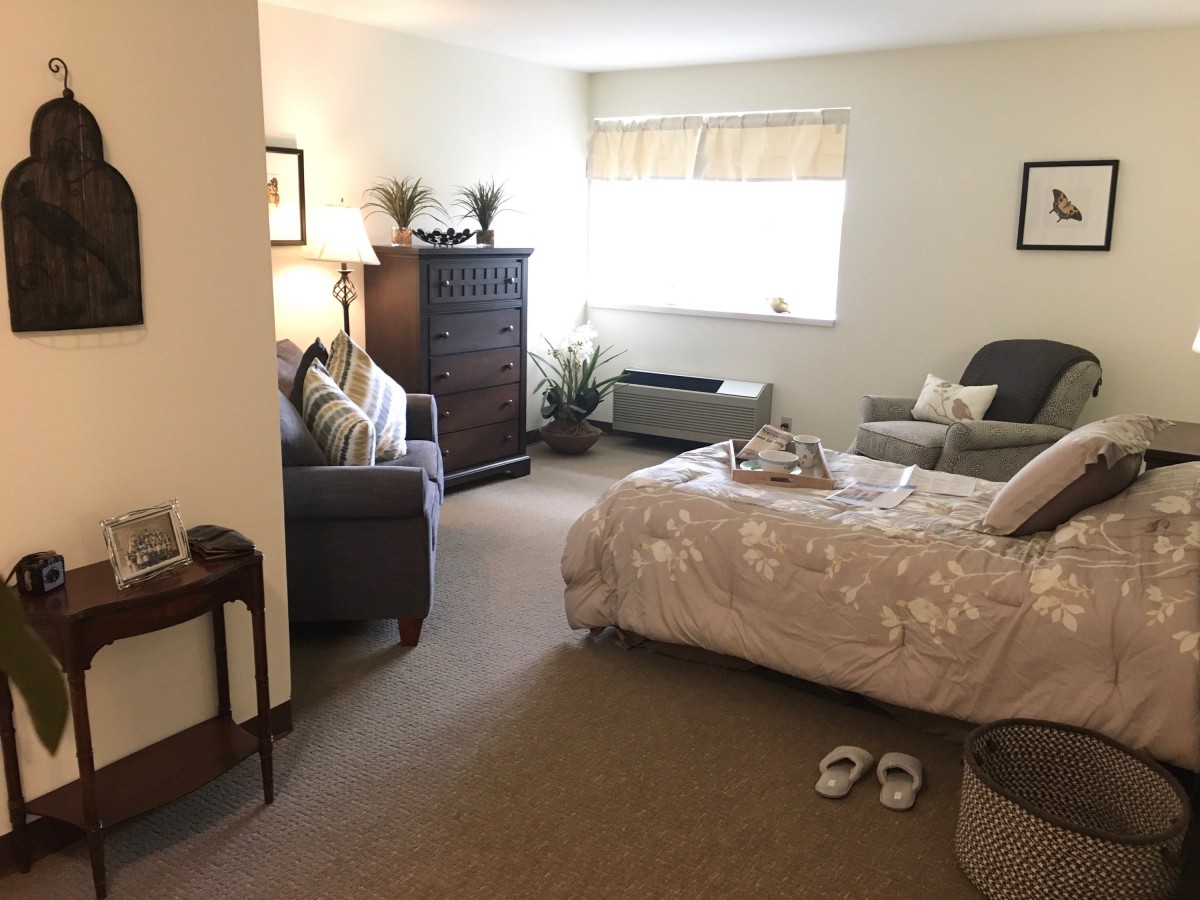 A cozy bedroom with a neatly made bed, armchair, and dresser.