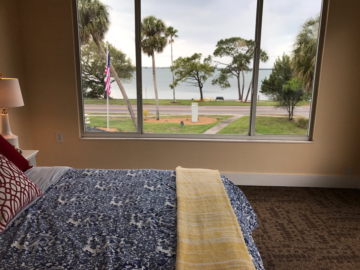 A cozy bedroom with a picturesque view of a lake and palm trees through the window.