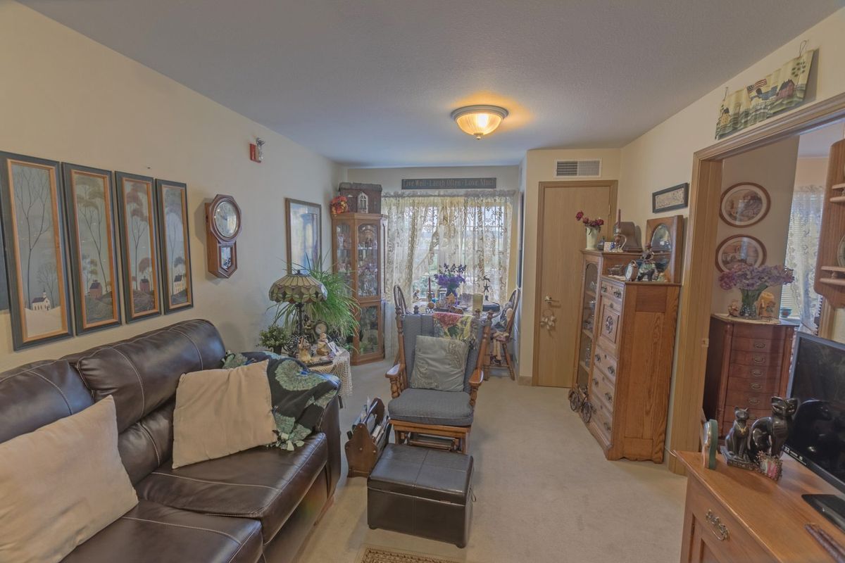 A cozy living room with a leather sofa, wooden furniture, and various decorative elements including plants and framed pictures.