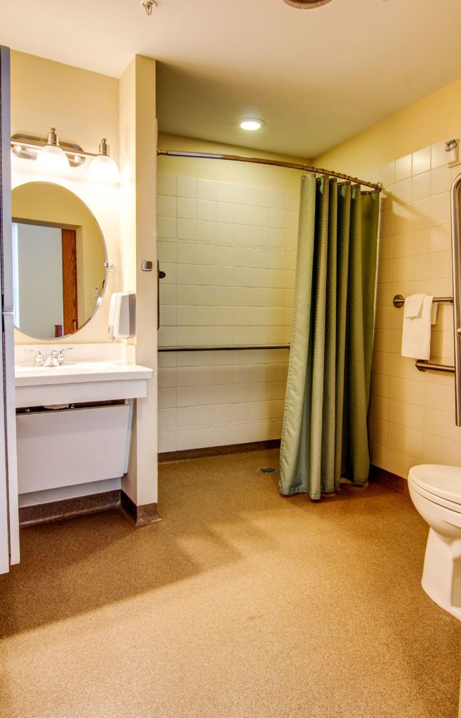 An accessible bathroom featuring a sink with a mirror, shower with curtain, and toilet with grab bars.