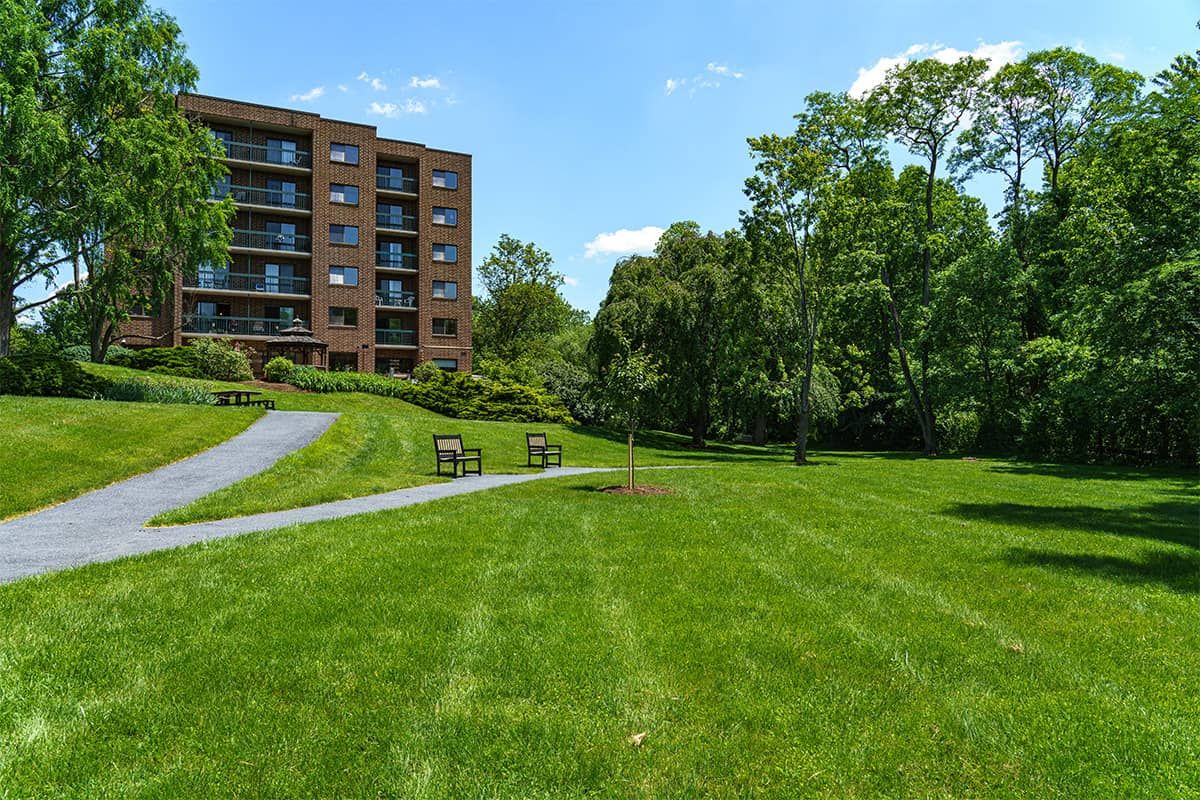 A sunny day with a view of a building surrounded by green grass, trees, and benches.