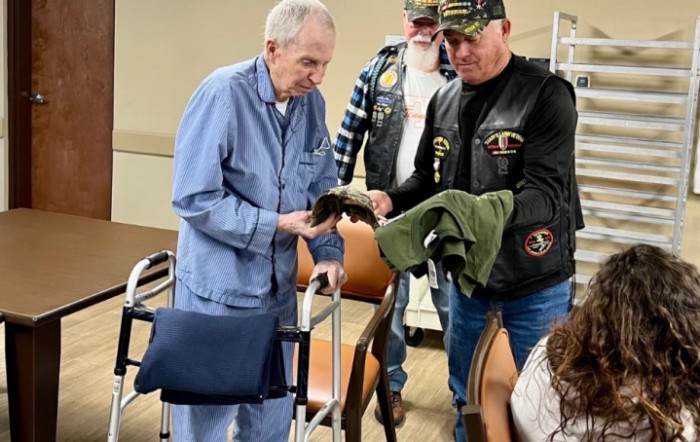 A group of veterans interacting, with one elderly man holding an item while another hands him a jacket.