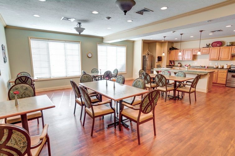 A brightly lit dining area with tables and chairs, adjacent to a kitchen.