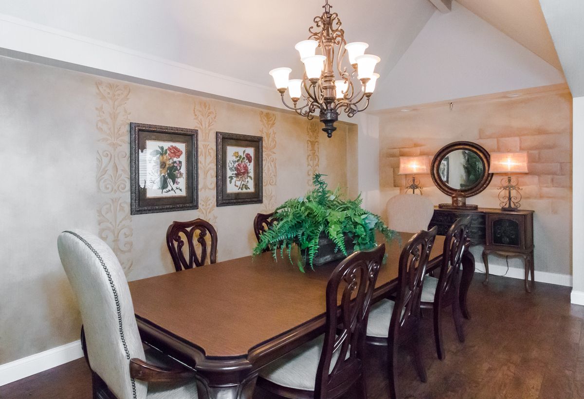 Elegant dining room with a wooden table, upholstered chairs, a central chandelier, and decorative wall elements.