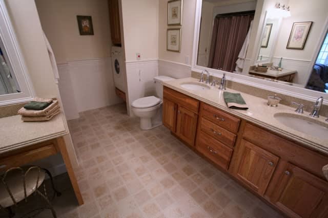 A clean and spacious bathroom featuring a large mirror, wooden cabinets, and tiled flooring.