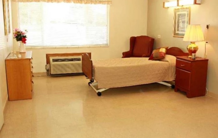 A simple hospital room with a single bed and an armchair next to a window.