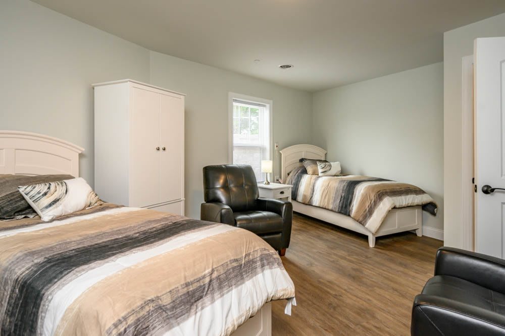 A spacious bedroom with two twin beds, featuring an armchair and a wardrobe.