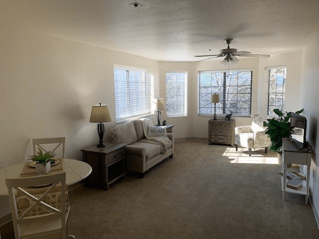A spacious living room filled with natural light, featuring a sofa, lamps, and several large windows.
