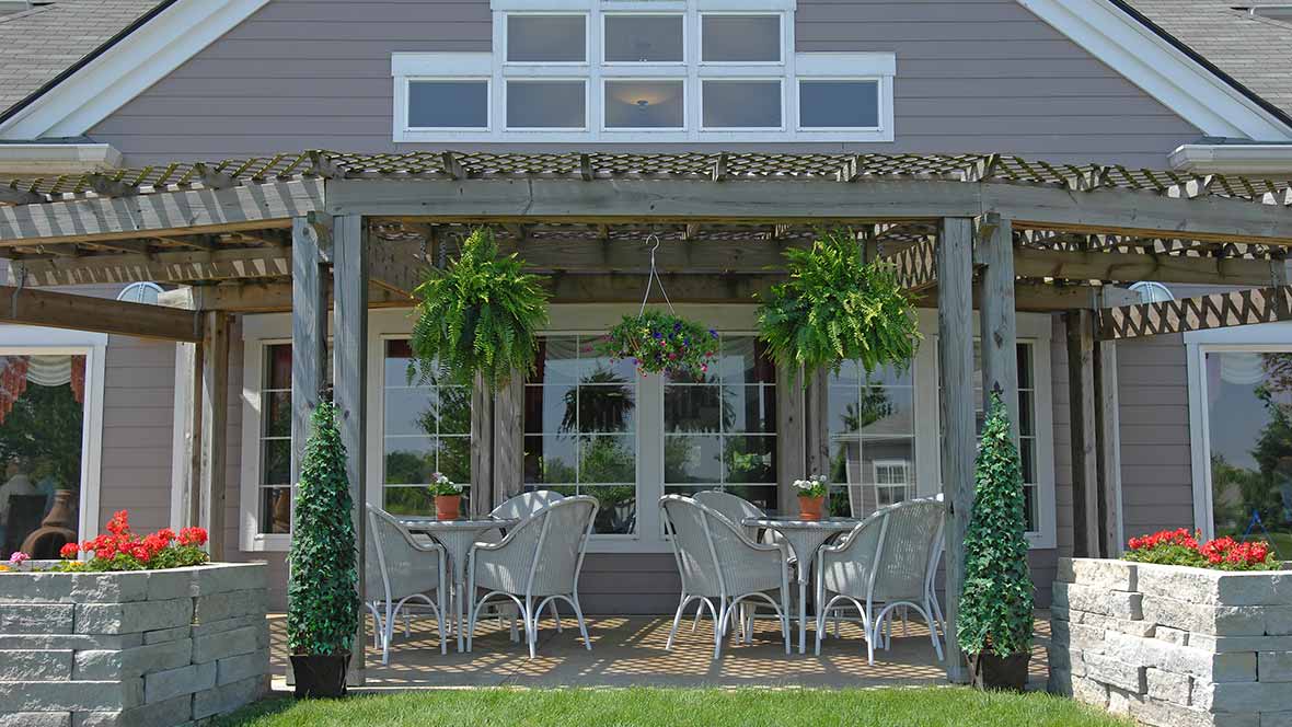 A cozy outdoor patio with wicker furniture and lush greenery under a pergola.