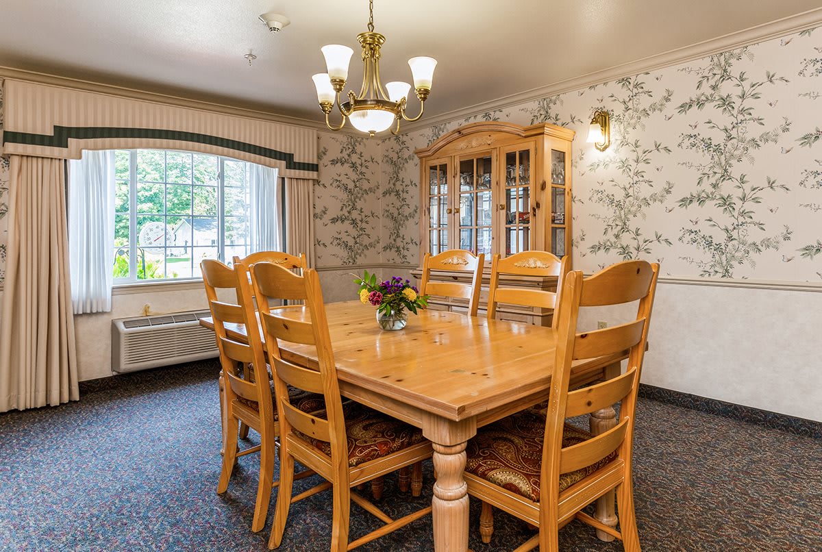 A cozy dining room with a wooden table and chairs, adorned with floral wallpaper and a classic chandelier.