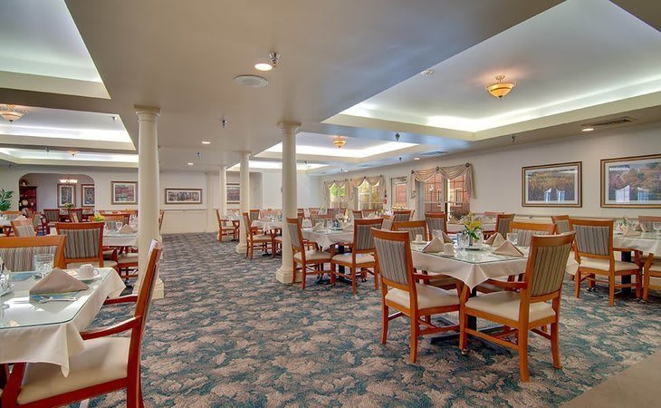 A spacious dining area featuring neatly arranged tables and chairs, with soft lighting and patterned carpeting.