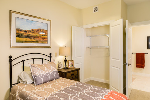 A cozy bedroom featuring a neatly made bed, a decorative lamp, and an open closet.