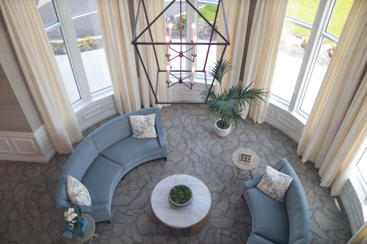 A stylish living room featuring curved sofas, a central coffee table with plants, and large windows allowing natural light.