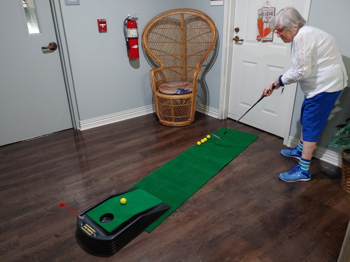 An elderly person playing mini golf indoors on a putting green.