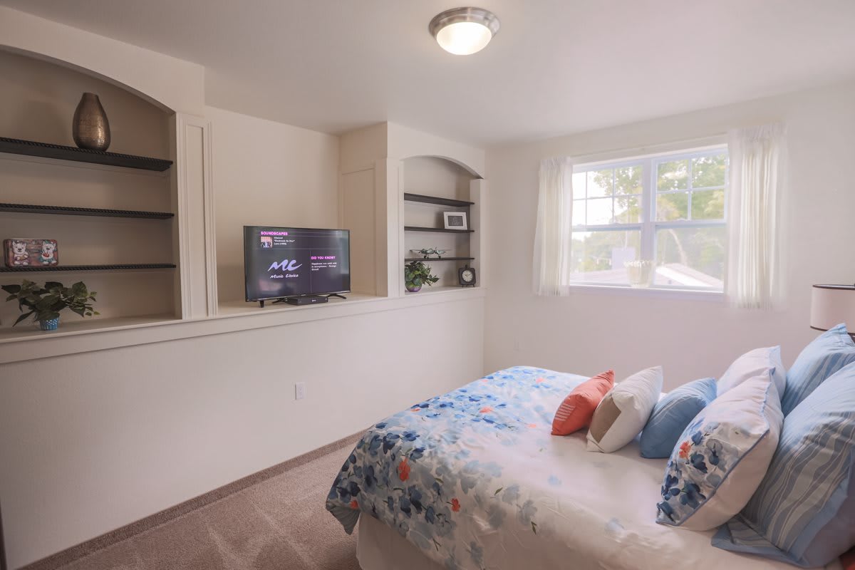 A cozy bedroom with built-in shelves, a television, and a bed adorned with colorful pillows.