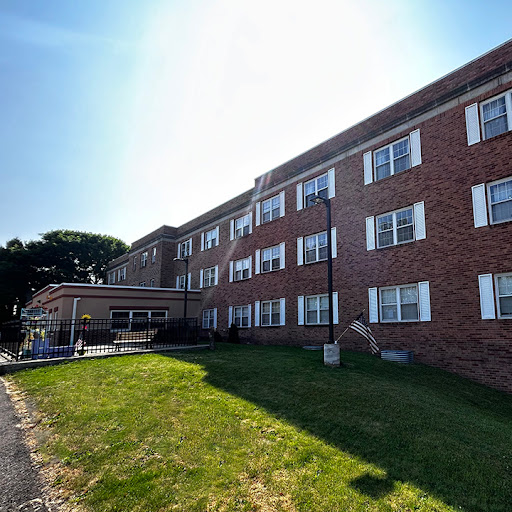 A brick apartment building basking in sunlight, surrounded by a grassy area.
