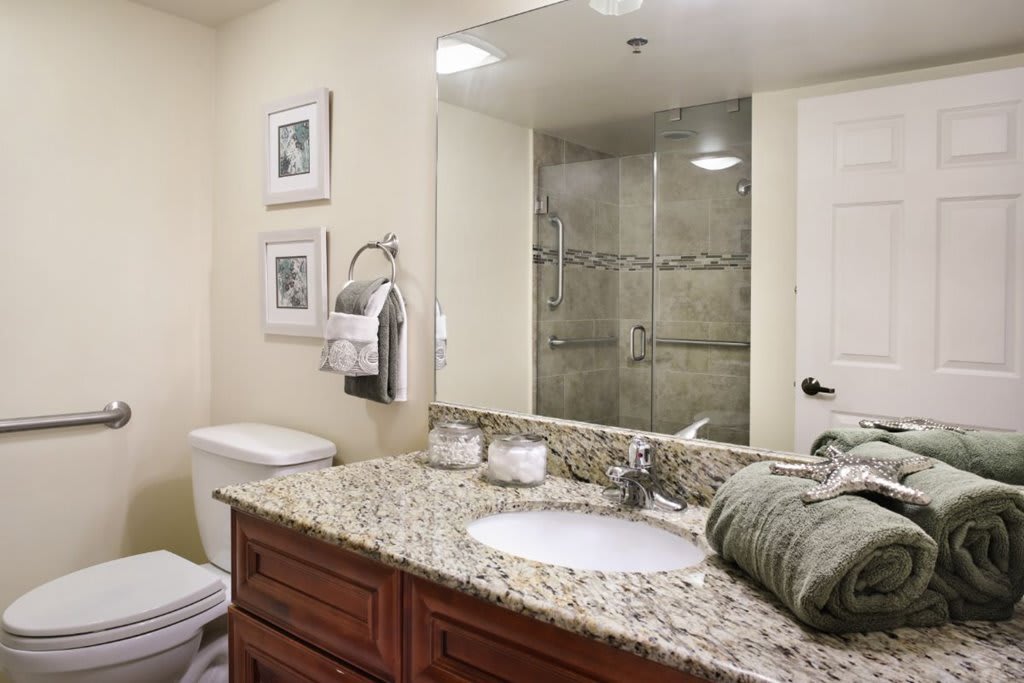 A modern bathroom with a granite countertop and glass shower enclosure.