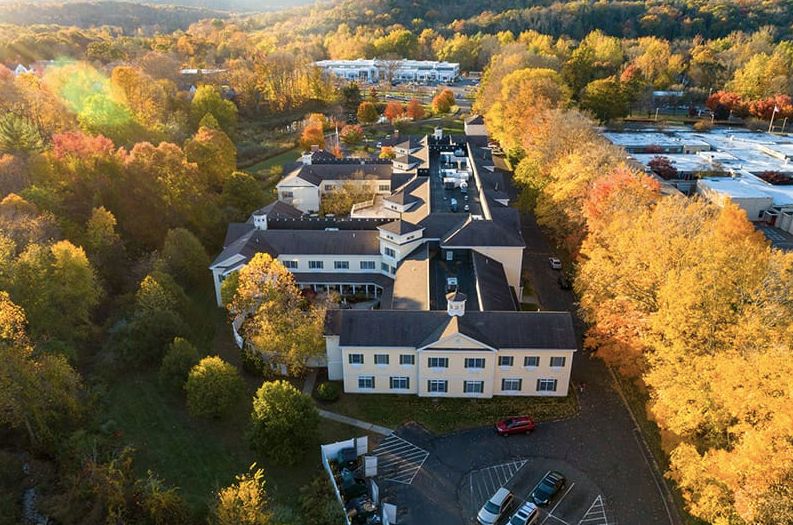 Aerial view of a building surrounded by autumn trees and a parking lot during sunset.