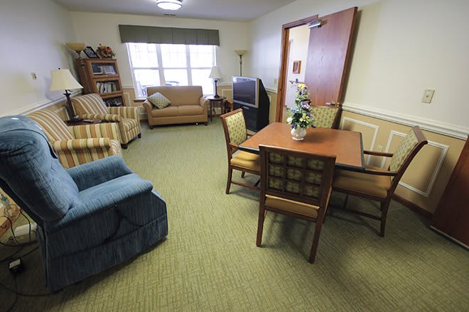 A cozy living room with a variety of furniture, including armchairs, a table with chairs, and a television.
