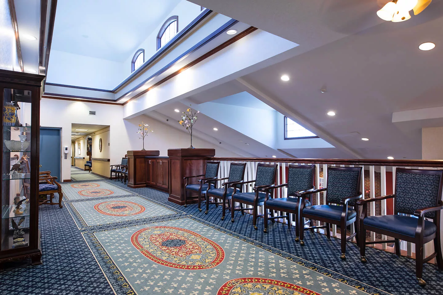 A well-lit hallway with a row of chairs and an intricately designed carpet.