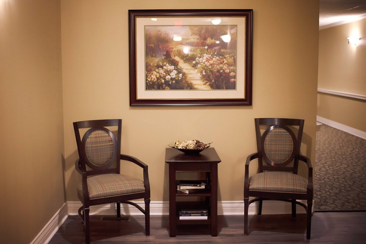 A cozy interior with two wooden chairs, a small table, and a framed wall painting.