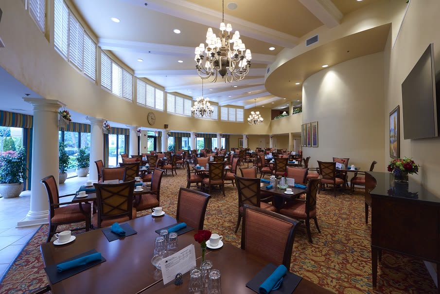 A spacious and elegant dining area featuring chandeliers, numerous tables, and comfortable seating.