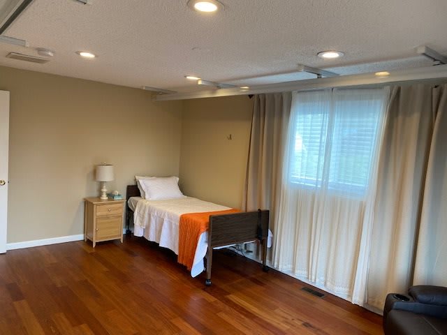 A minimalist bedroom with a single bed, wooden floors, and soft lighting.