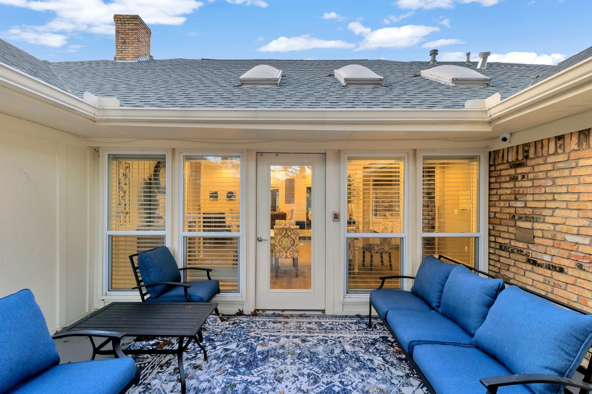 A cozy outdoor patio with blue cushioned seating and a glass door leading inside.
