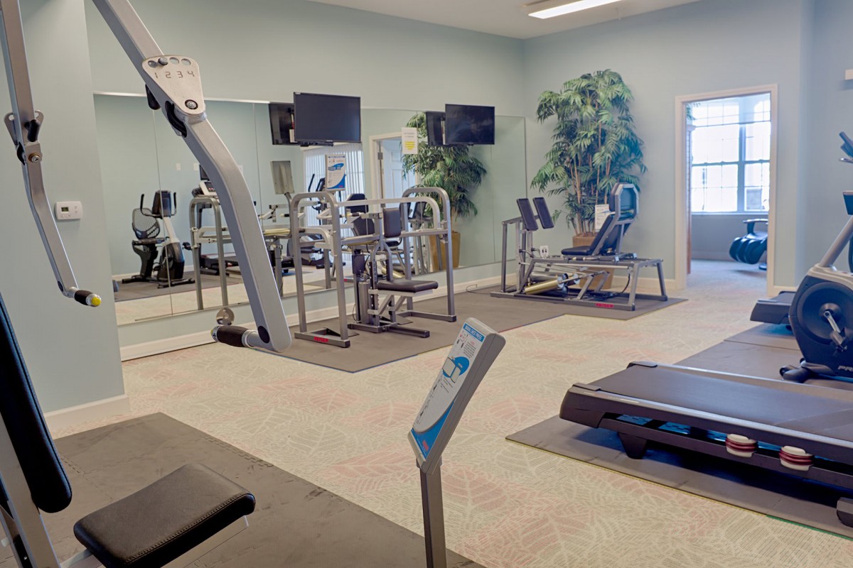 A clean and well-equipped gym with various exercise machines and mirrors.