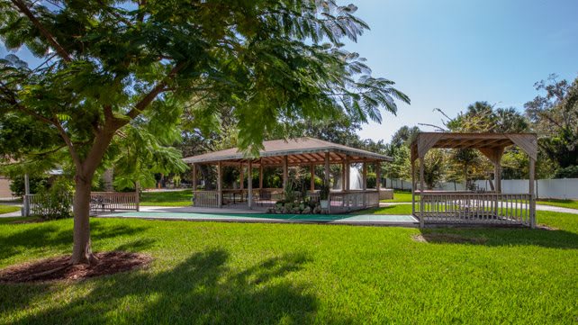 A serene park setting featuring a gazebo surrounded by lush greenery and trees under a clear, sunny sky.