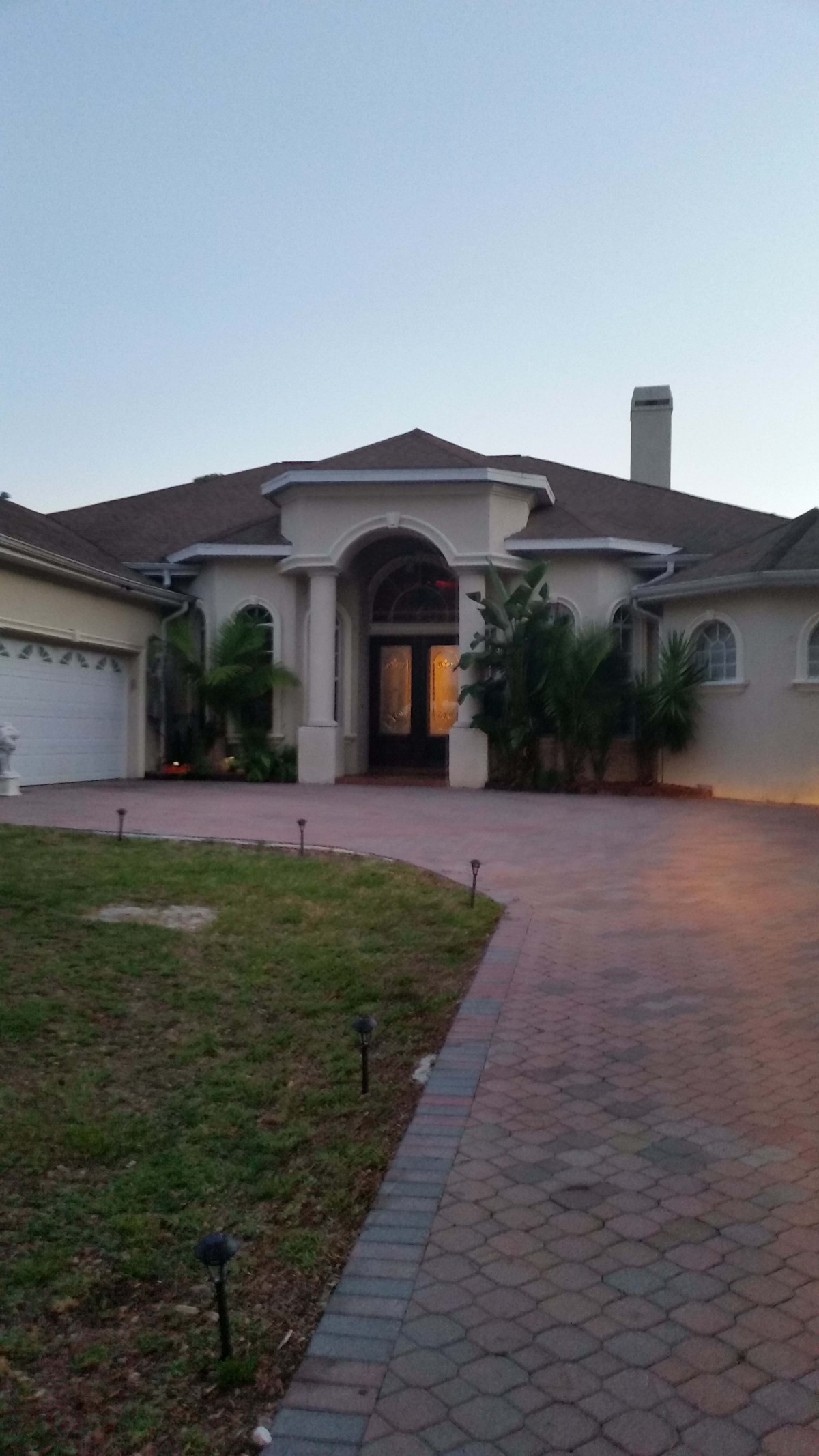A view of a large, single-story house with a paved driveway and surrounding greenery.