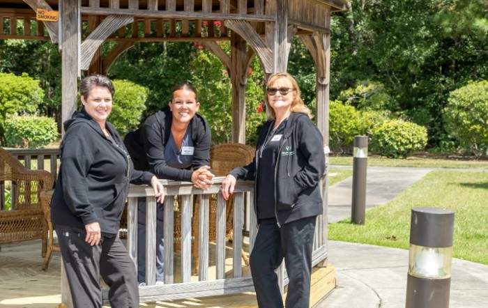 Three people standing and leaning on a gazebo in a sunny outdoor setting.