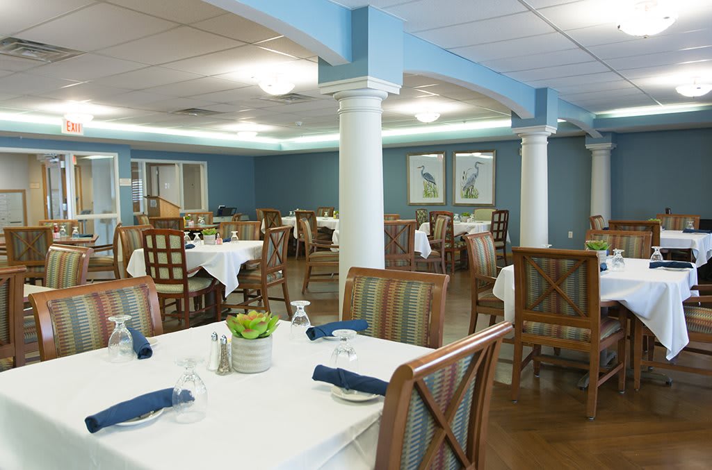 A well-arranged dining area with neatly set tables and wooden chairs, featuring blue walls and elegant decor.