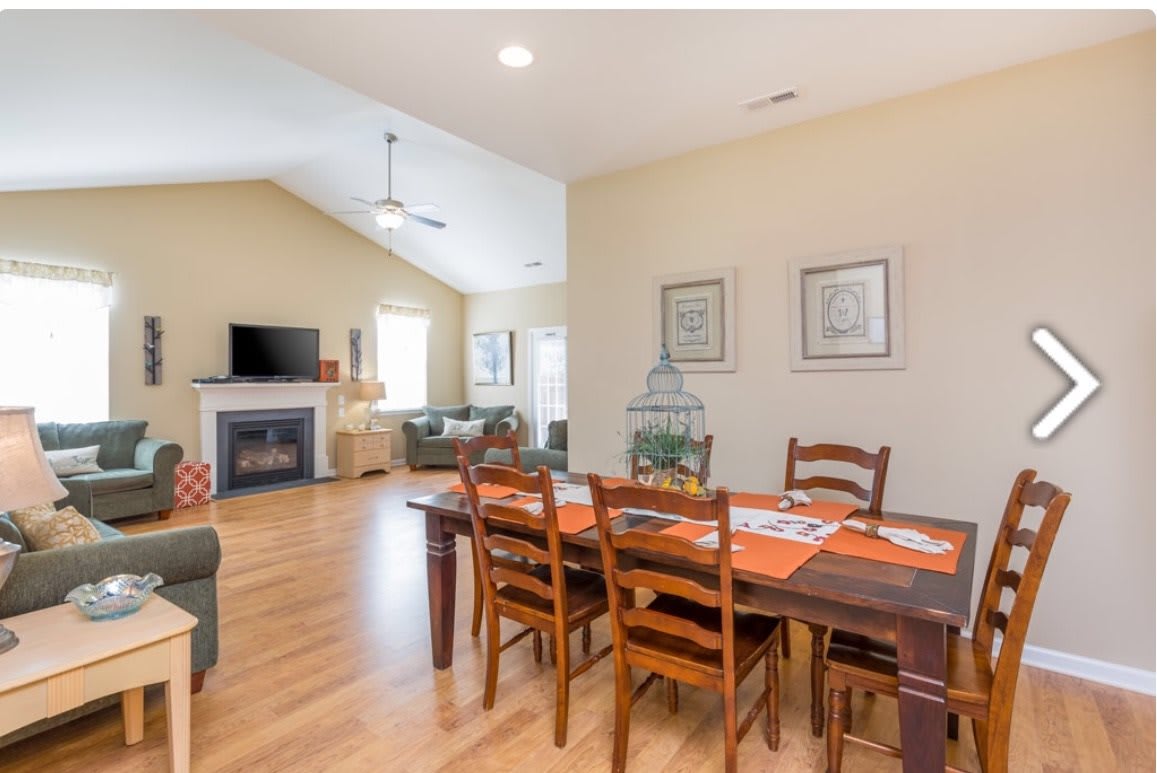 A spacious living and dining area with an open floor plan, featuring wooden flooring, a cozy fireplace, and stylish furniture.
