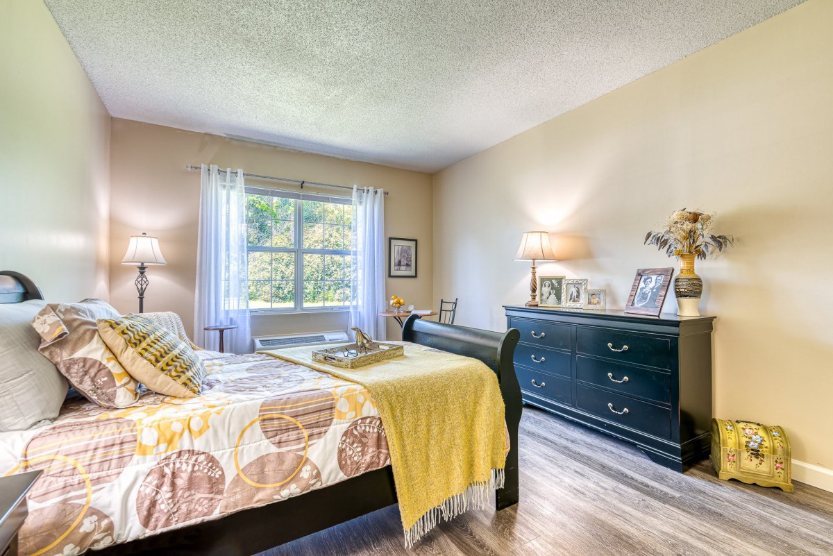 A cozy bedroom with a sleigh bed, dresser, and large window letting in natural light.