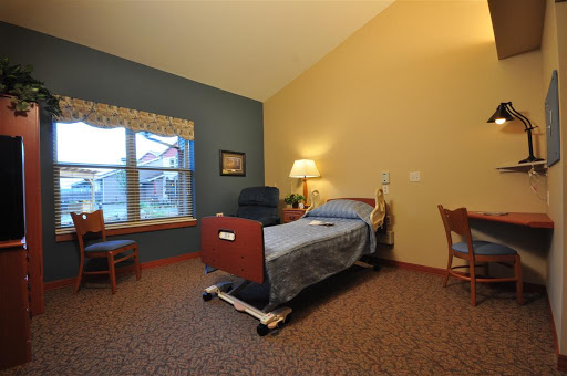 A cozy hospital room featuring a bed, chairs, and natural light from the window.