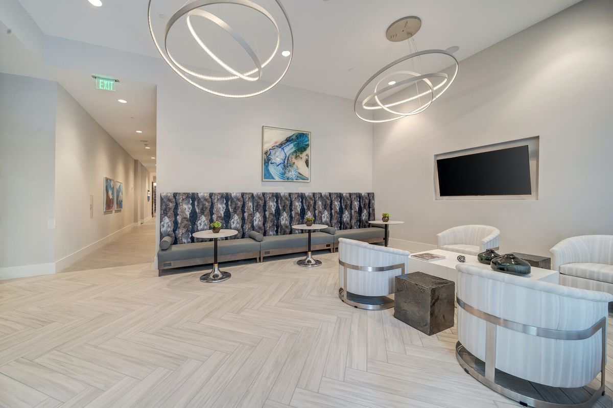 A sleek and modern waiting area featuring a long upholstered seating arrangement, stylish light fixtures, and contemporary artwork on the wall.