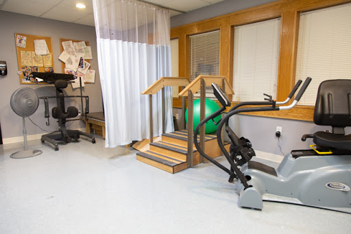 A well-equipped therapy room featuring a set of stairs for rehabilitation exercises, an exercise bike, and a green exercise ball.