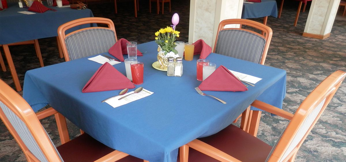 A neatly set dining table with red napkins, drinks, and a floral centerpiece.