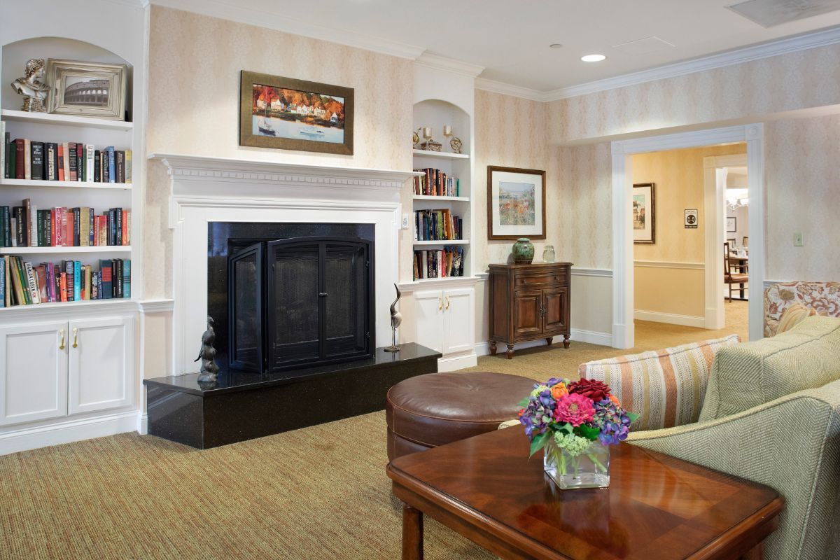 A cozy living room with a fireplace, bookshelf, and a vase of flowers on the table.