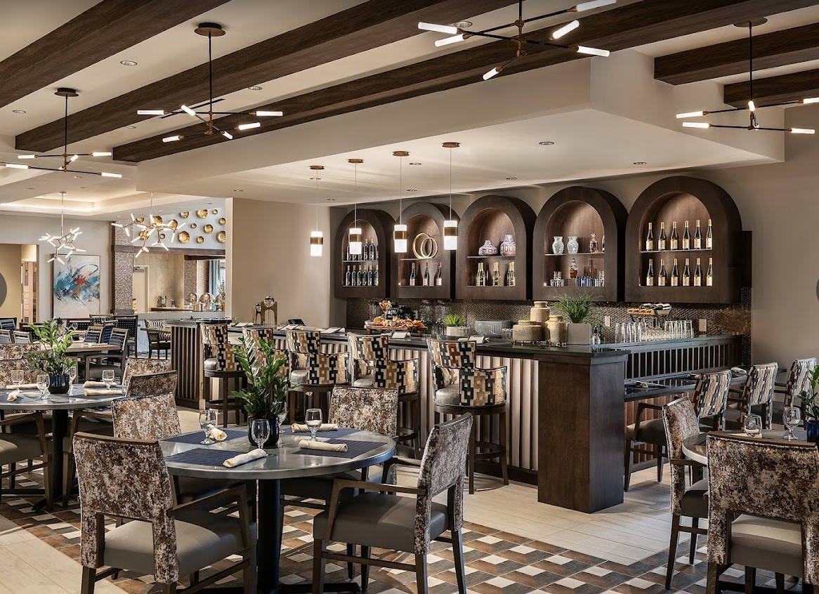 A modern restaurant interior featuring a bar area with decorative lighting and elegantly set tables.