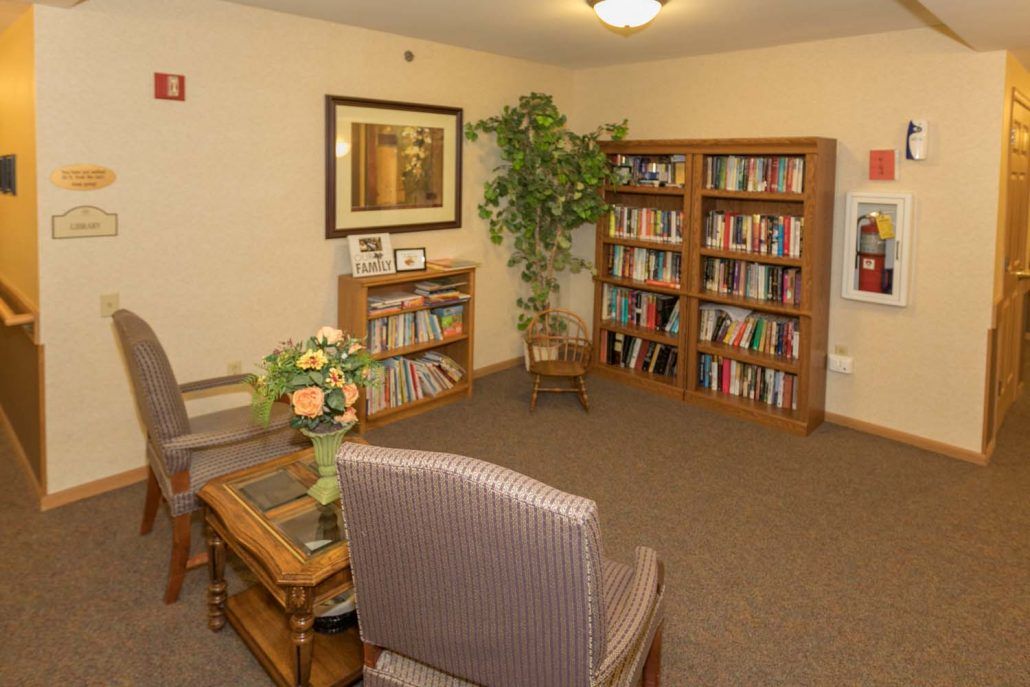 A cozy reading room with bookshelves, comfortable chairs, and a potted plant.